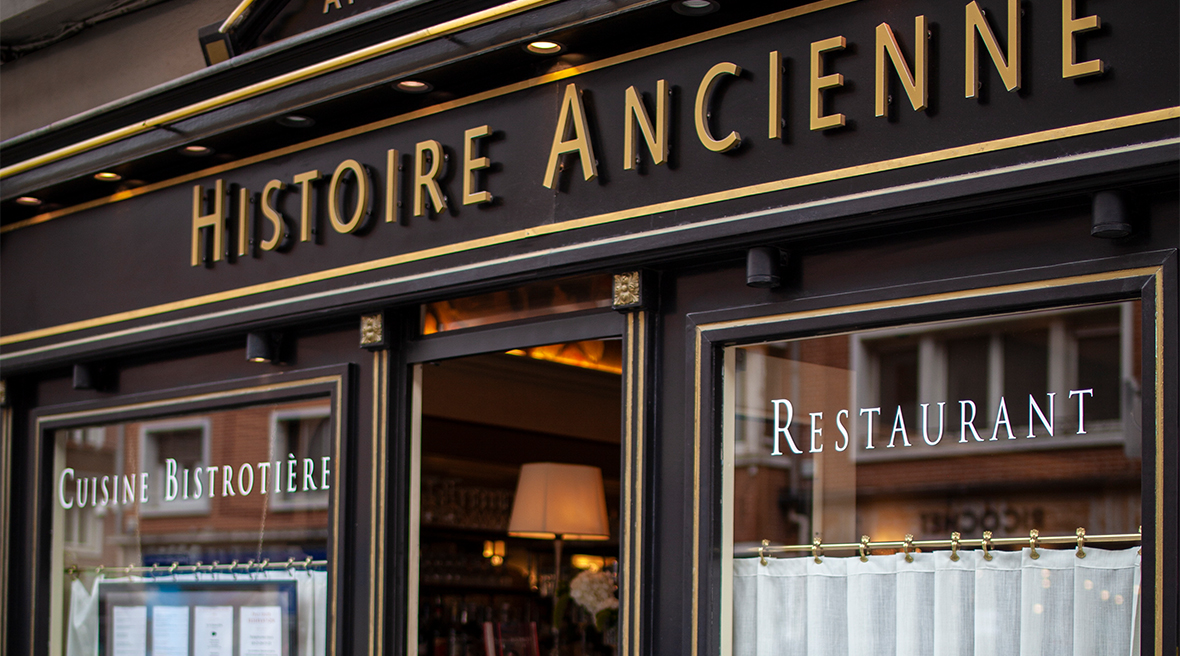 The front of a brasserie restaurant with a door in the middle of two big windows, dark brown surround and the words Histoire Ancienne above the door in gold block capitals